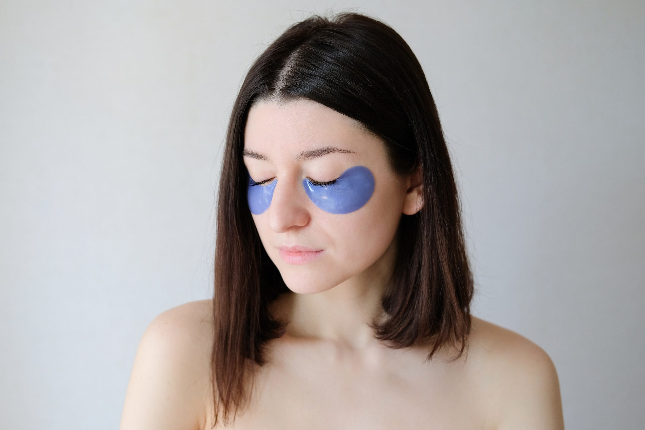 Beautiful woman with closed eyes applying under eye patches for